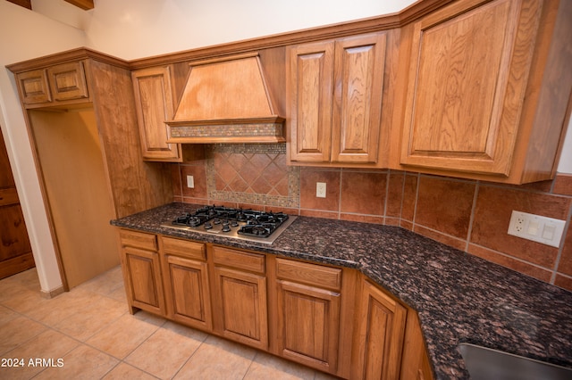 kitchen featuring custom range hood, stainless steel gas stovetop, backsplash, and dark stone countertops
