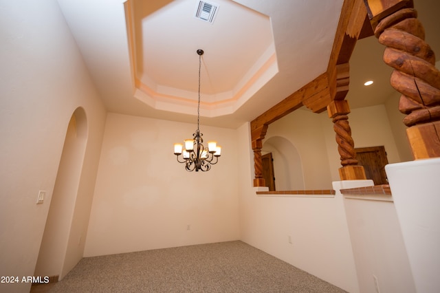 unfurnished room featuring a raised ceiling, an inviting chandelier, and carpet floors