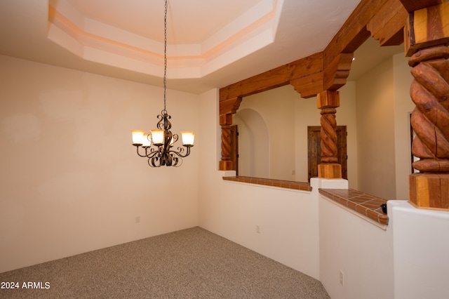 carpeted spare room featuring a notable chandelier and a tray ceiling