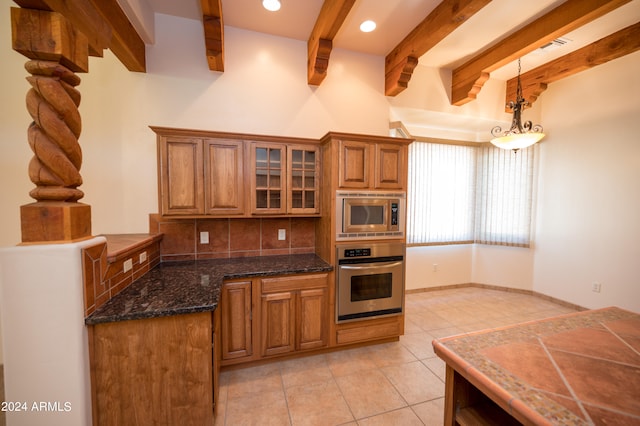 kitchen featuring dark stone counters, tasteful backsplash, appliances with stainless steel finishes, light tile floors, and pendant lighting