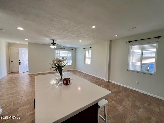 kitchen with ceiling fan, a kitchen breakfast bar, a center island, and a textured ceiling