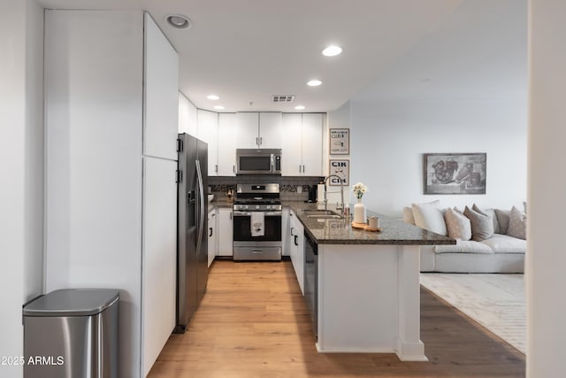 kitchen featuring kitchen peninsula, stainless steel appliances, light wood-type flooring, white cabinets, and sink