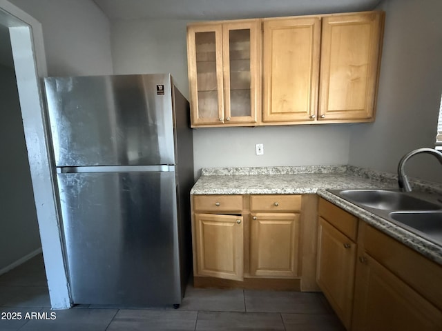 kitchen featuring glass insert cabinets, freestanding refrigerator, a sink, and light tile patterned floors