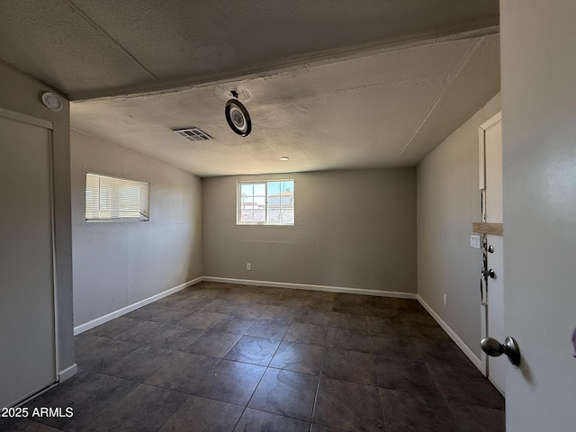 empty room featuring visible vents, a textured ceiling, and baseboards