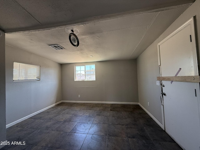 empty room featuring a textured ceiling, visible vents, and baseboards