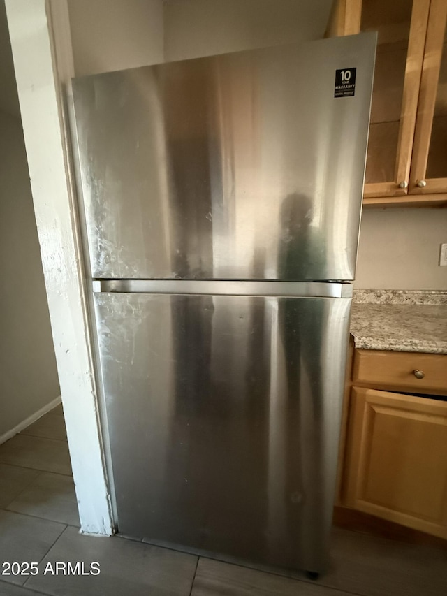 details featuring glass insert cabinets, freestanding refrigerator, and brown cabinets