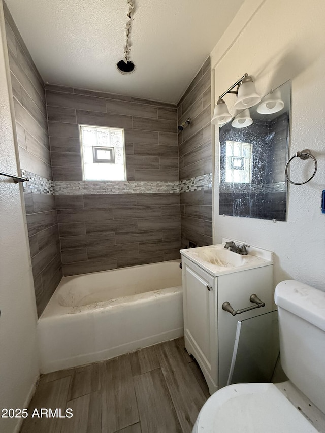 full bath featuring a textured ceiling, toilet, wood finished floors, vanity, and shower / washtub combination