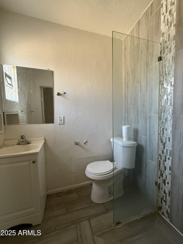 bathroom with a textured wall, vanity, toilet, and walk in shower