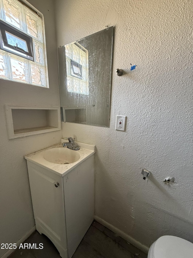 bathroom featuring a textured wall, vanity, and toilet