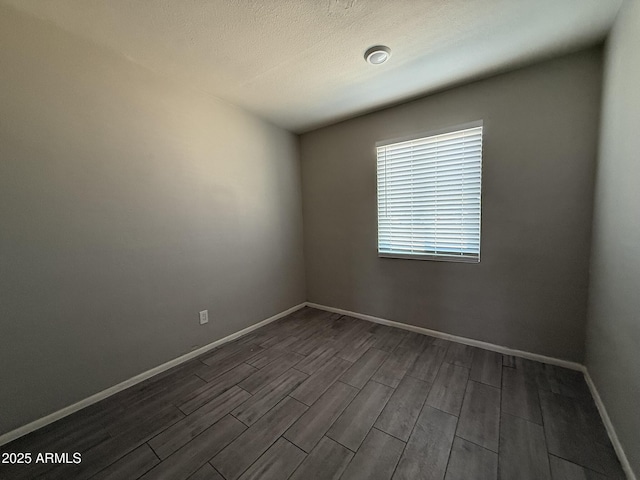 spare room with a textured ceiling, baseboards, and dark wood-type flooring