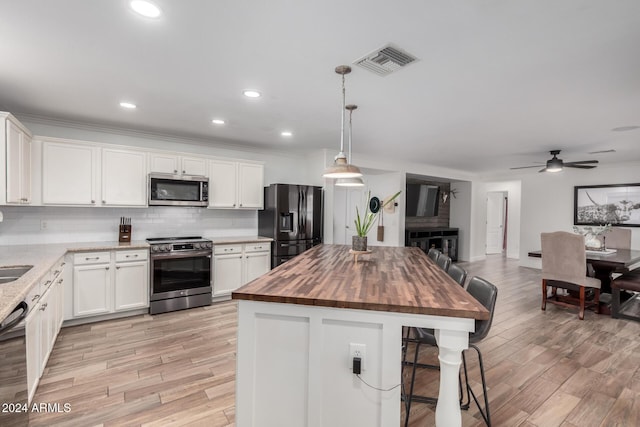 kitchen with hanging light fixtures, stainless steel appliances, a kitchen island, wood counters, and white cabinets