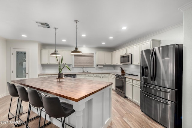 kitchen featuring a center island, sink, appliances with stainless steel finishes, decorative light fixtures, and butcher block counters