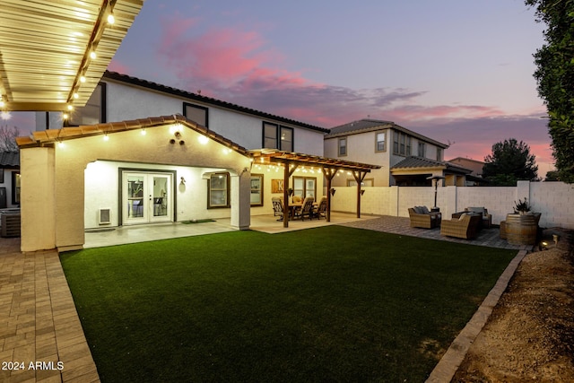 back house at dusk featuring outdoor lounge area, a patio area, a lawn, and french doors