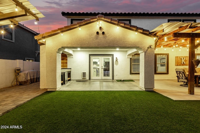 back house at dusk featuring french doors, a yard, and a patio area