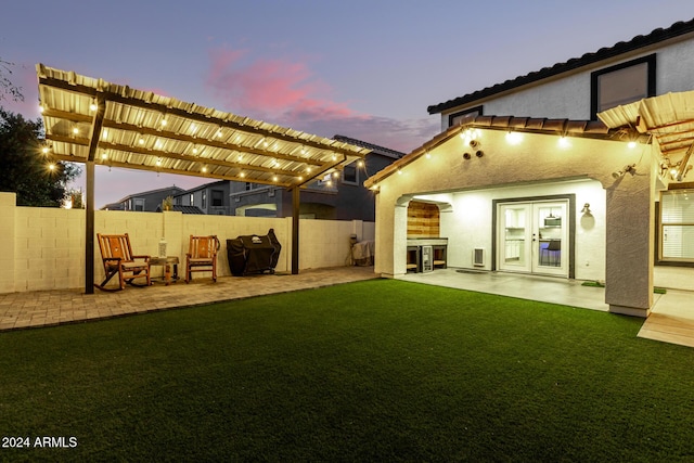 back house at dusk with french doors, a pergola, a patio area, and a lawn