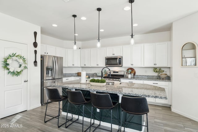 kitchen with appliances with stainless steel finishes, white cabinetry, light stone counters, and hanging light fixtures