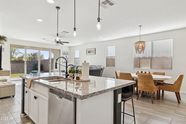 kitchen with a center island with sink, dishwasher, pendant lighting, and white cabinetry