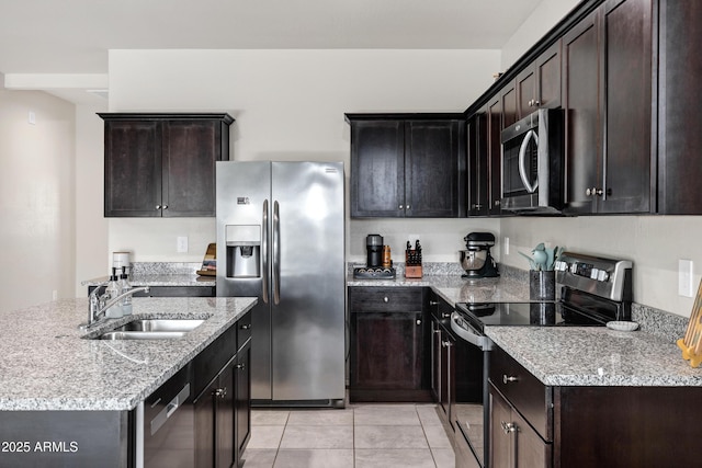 kitchen with a kitchen island with sink, a sink, stainless steel appliances, light tile patterned floors, and light stone countertops