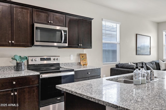 kitchen featuring light stone counters, dark brown cabinets, open floor plan, and stainless steel appliances