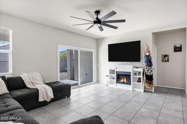 living area featuring a glass covered fireplace, light tile patterned floors, baseboards, and ceiling fan