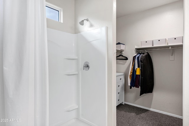 bathroom with a walk in closet, baseboards, and a stall shower