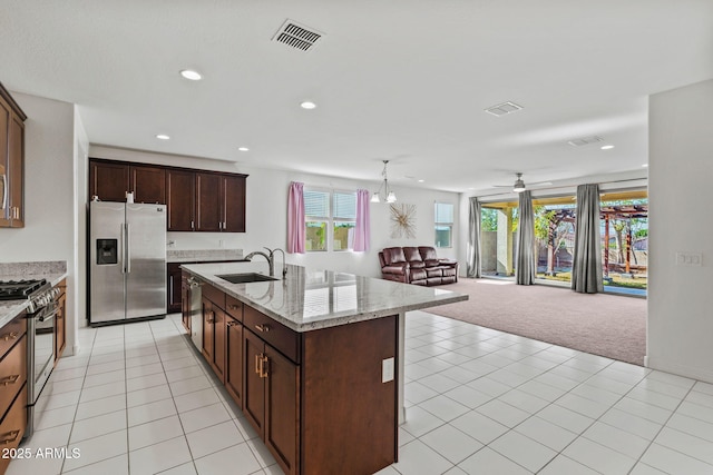 kitchen featuring light stone counters, stainless steel appliances, open floor plan, a kitchen island with sink, and a sink