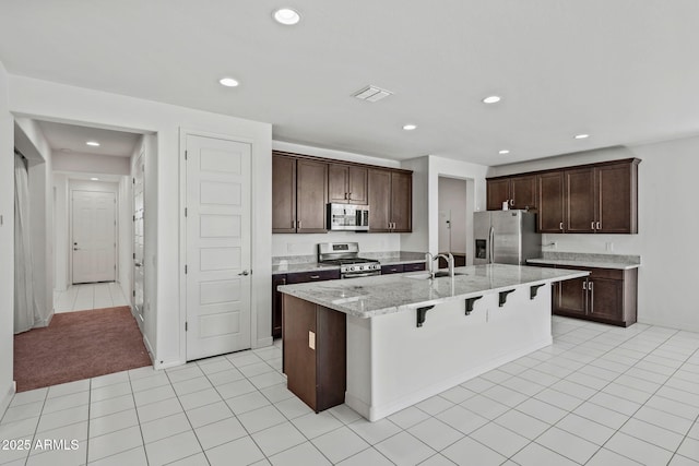 kitchen with dark brown cabinetry, visible vents, a breakfast bar, a kitchen island with sink, and stainless steel appliances