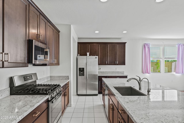 kitchen with recessed lighting, stainless steel appliances, a sink, dark brown cabinets, and light stone countertops