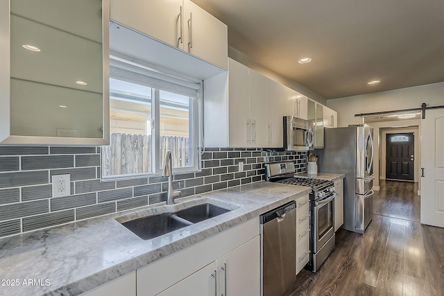 kitchen featuring appliances with stainless steel finishes, dark wood finished floors, a sink, light stone counters, and white cabinetry
