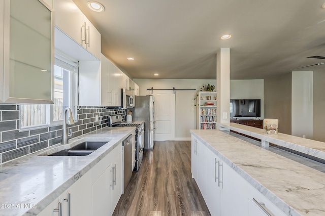 kitchen with white cabinets, appliances with stainless steel finishes, a barn door, a sink, and dark wood-style floors