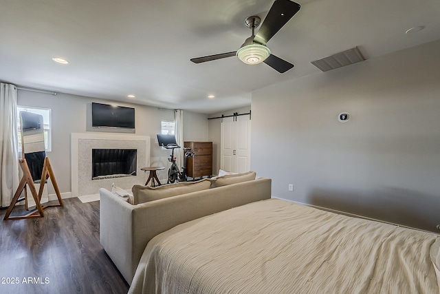 bedroom with visible vents, dark wood-style flooring, a fireplace, baseboards, and a barn door