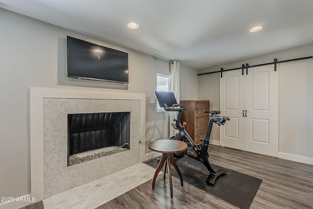 workout room featuring a barn door, a fireplace with flush hearth, recessed lighting, and wood finished floors