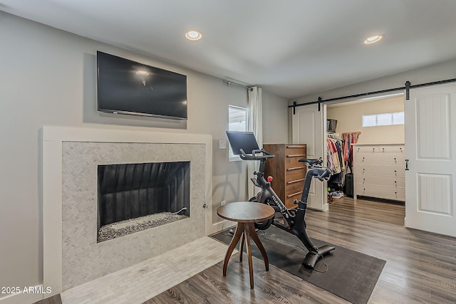 exercise room featuring recessed lighting, a barn door, wood finished floors, and a tiled fireplace