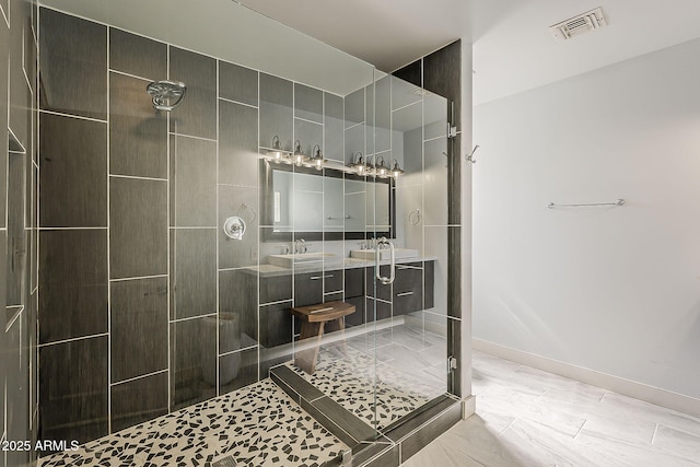 bathroom featuring visible vents, double vanity, baseboards, and a tile shower