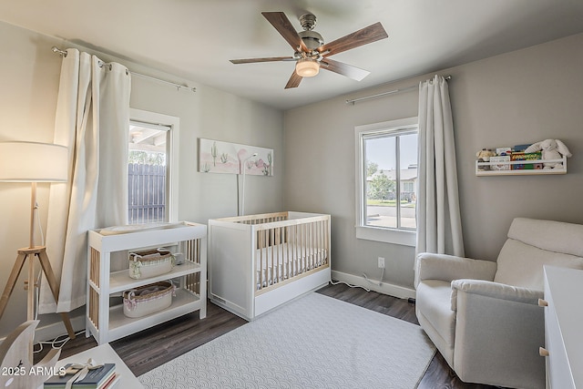 bedroom featuring baseboards, a crib, wood finished floors, and multiple windows