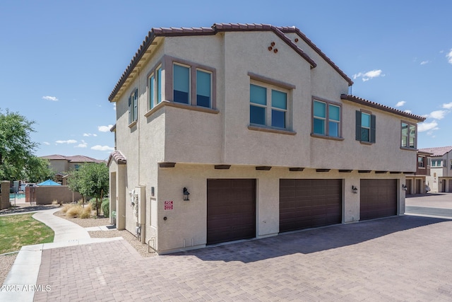exterior space with stucco siding, an attached garage, decorative driveway, and a tile roof