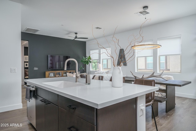 kitchen with ceiling fan, a sink, light countertops, a kitchen island with sink, and visible vents