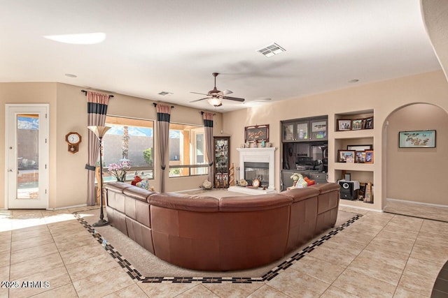 living area featuring a glass covered fireplace, built in shelves, baseboards, and tile patterned flooring