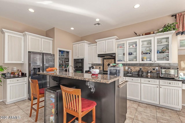 kitchen featuring under cabinet range hood, dobule oven black, a kitchen bar, refrigerator with ice dispenser, and backsplash