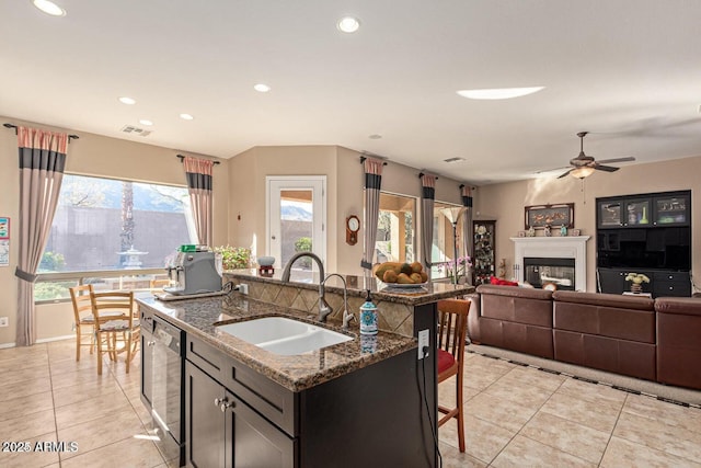 kitchen featuring visible vents, a sink, a kitchen breakfast bar, a glass covered fireplace, and dishwasher