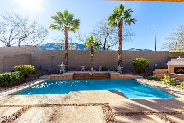 view of pool featuring a fenced in pool, exterior fireplace, a fenced backyard, a patio area, and a mountain view