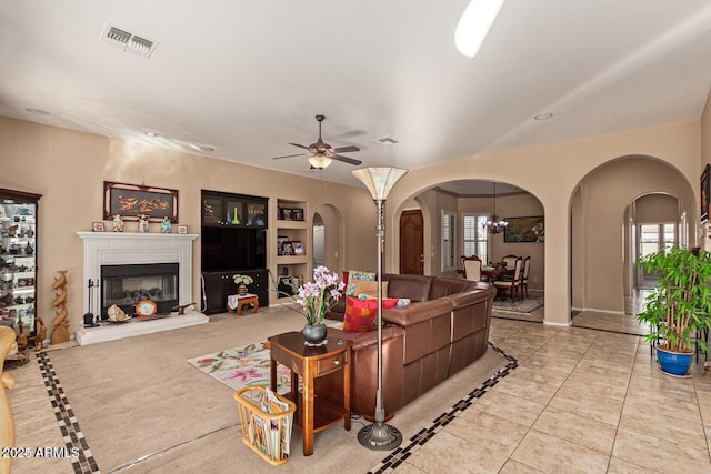 living area with ceiling fan, visible vents, arched walkways, and a glass covered fireplace