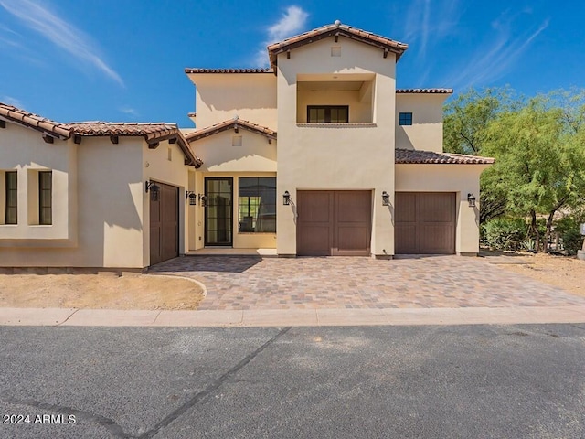 mediterranean / spanish house featuring an attached garage, a tiled roof, decorative driveway, and stucco siding