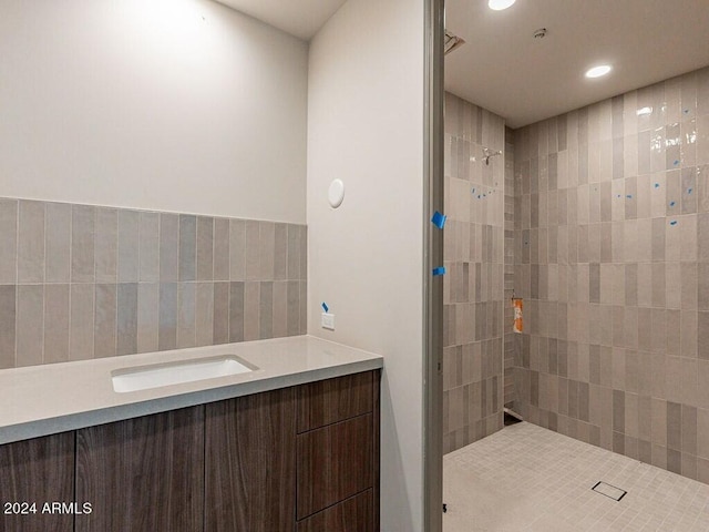 bathroom with tile walls, a tile shower, and vanity