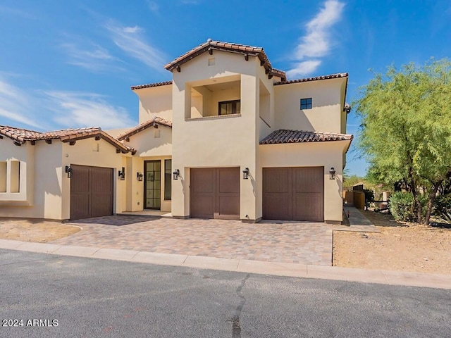 mediterranean / spanish-style house with a garage, decorative driveway, a tiled roof, and stucco siding