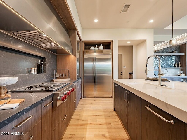 kitchen featuring a sink, visible vents, appliances with stainless steel finishes, wall chimney exhaust hood, and light wood finished floors