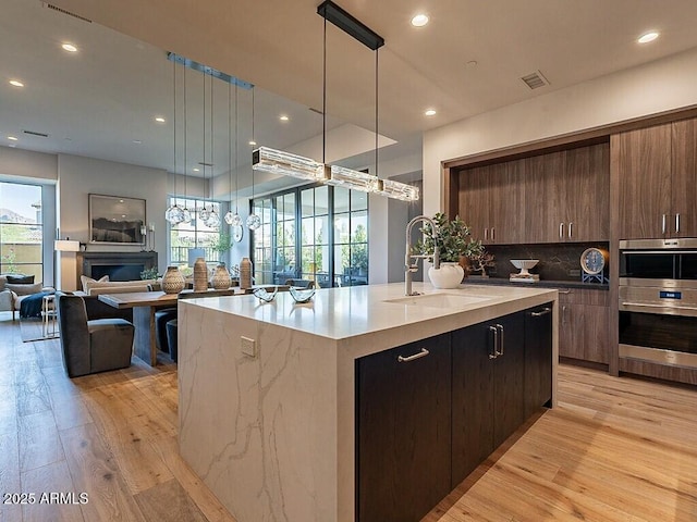 kitchen with light wood-style flooring, modern cabinets, a sink, and a kitchen island with sink