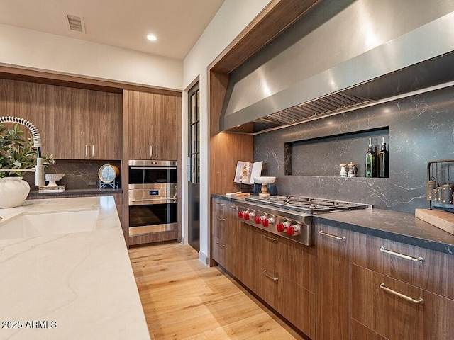 kitchen featuring light wood finished floors, visible vents, appliances with stainless steel finishes, stone counters, and wall chimney range hood