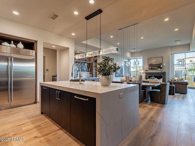 kitchen featuring visible vents, modern cabinets, light wood-type flooring, a sink, and built in fridge