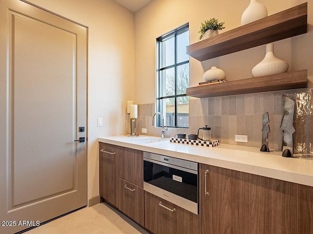 kitchen with light countertops, a sink, backsplash, and open shelves